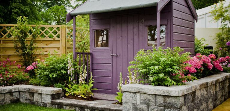 A beautiful tidy storage shed surrounded by plants and blooming flowers.