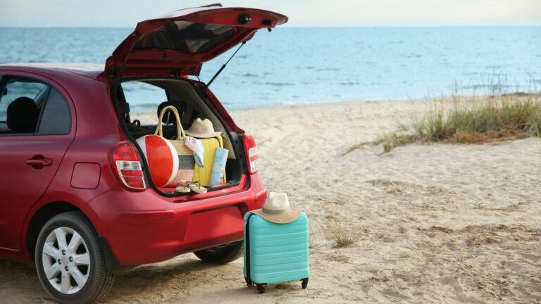 The trunk of a family van is open, with a beach visible in the background. The trunk would be more tidy with summer organizing solutions.